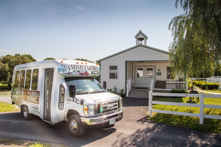White tour van in front of a small building with a bell tower and green lawn.