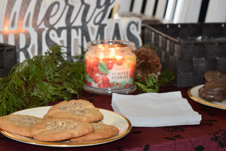 Cookies and candle on table with 'Merry Christmas' sign, greenery, and napkins.