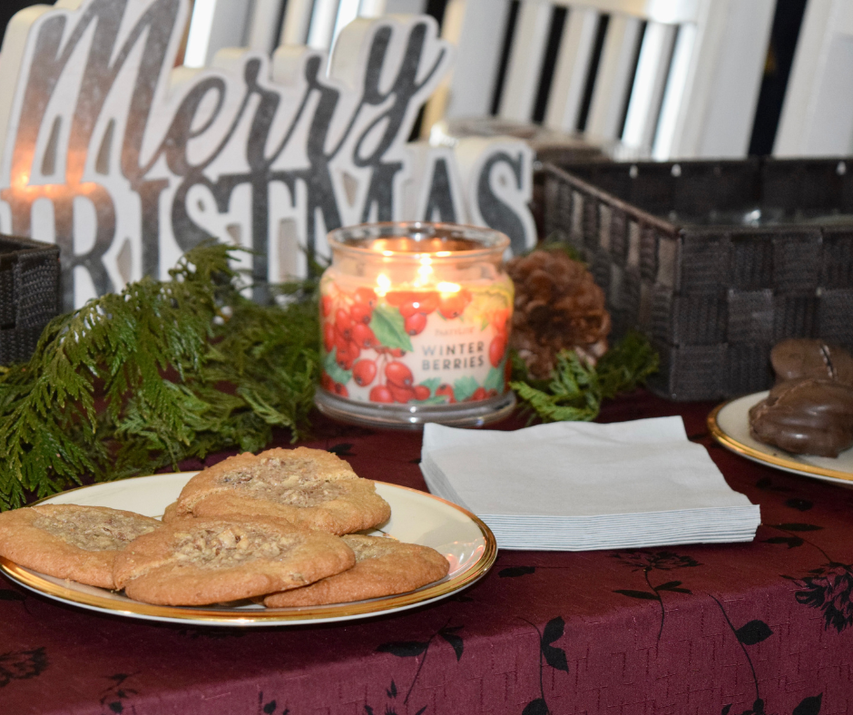 Cookies and candle on table with 'Merry Christmas' sign, greenery, and napkins.
