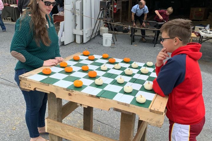 Woman and boy playing checkers with small pumpkins on a large outdoor board.
