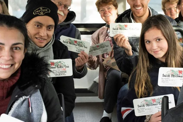 Group of people in a bus holding Amish Christmas cookie tour tickets, smiling.
