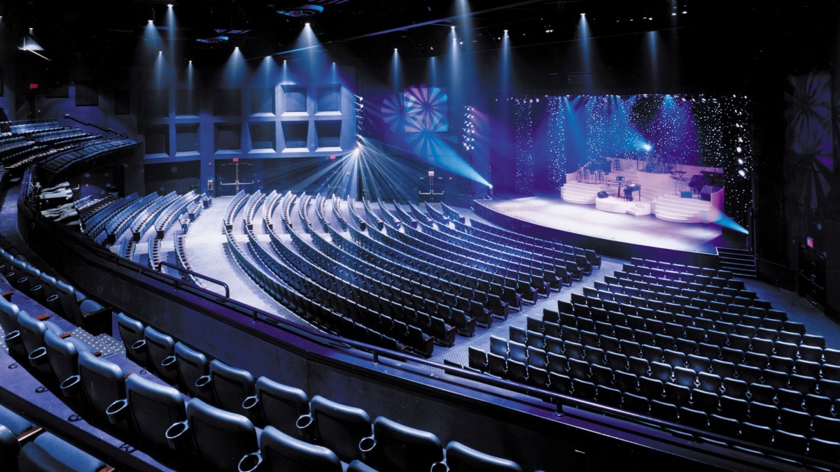 Empty theater with curved seating and illuminated stage with spotlights.